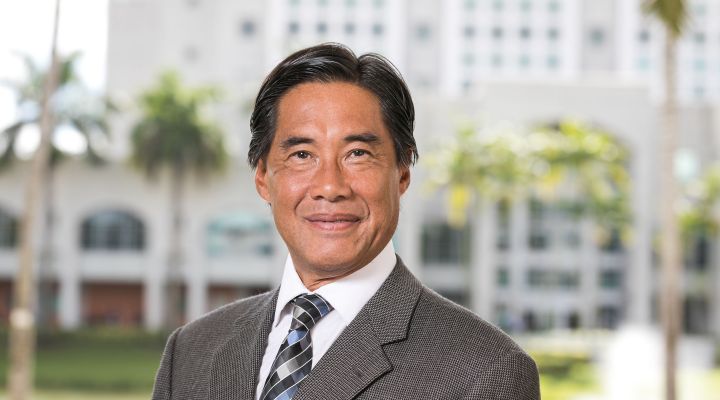 Steven Lee standing in a suit in front of a building and palm trees