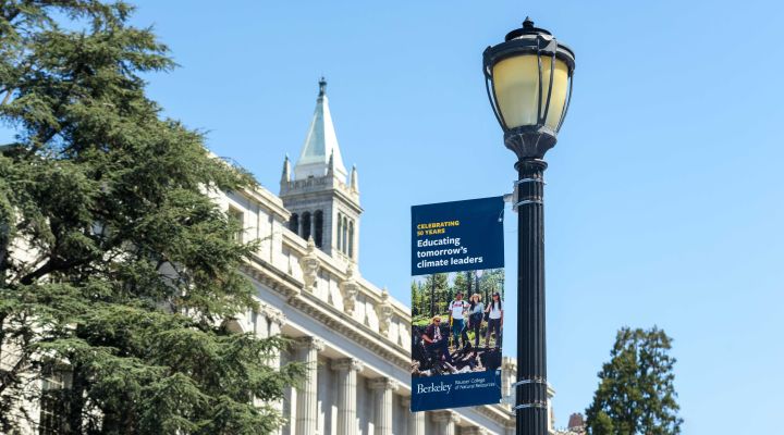 A lightpole banner with a picture of researchers in the field and the UC Berkeley campanile in the background